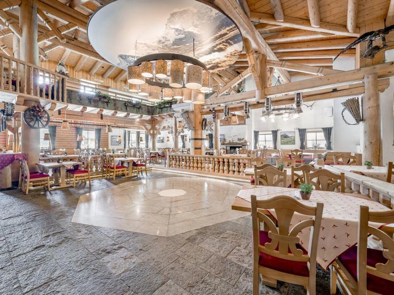 Ruime rustieke eetzaal met houten balken, tafels en stoelen in landelijke stijl.