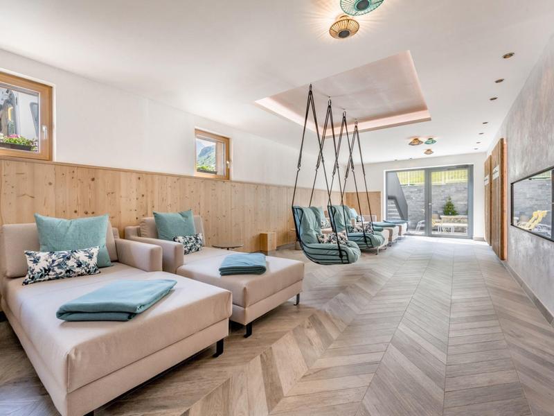 Lichte lounge met houten wandbekleding, fauteuils en moderne hangstoelen met uitzicht op terras.