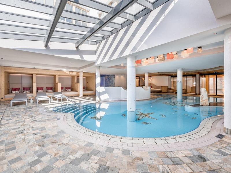 Licht overdekt zwembad met glazen dak, zuilen en comfortabele zitgedeeltes.