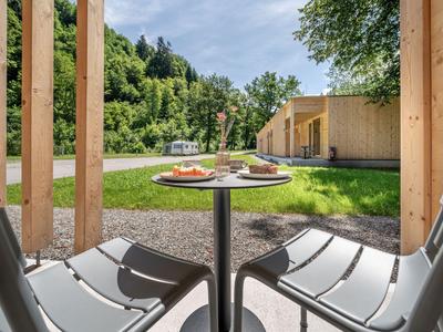 Balcony table with breakfast overlooking a green lawn and wooden buildings on a sunny day.