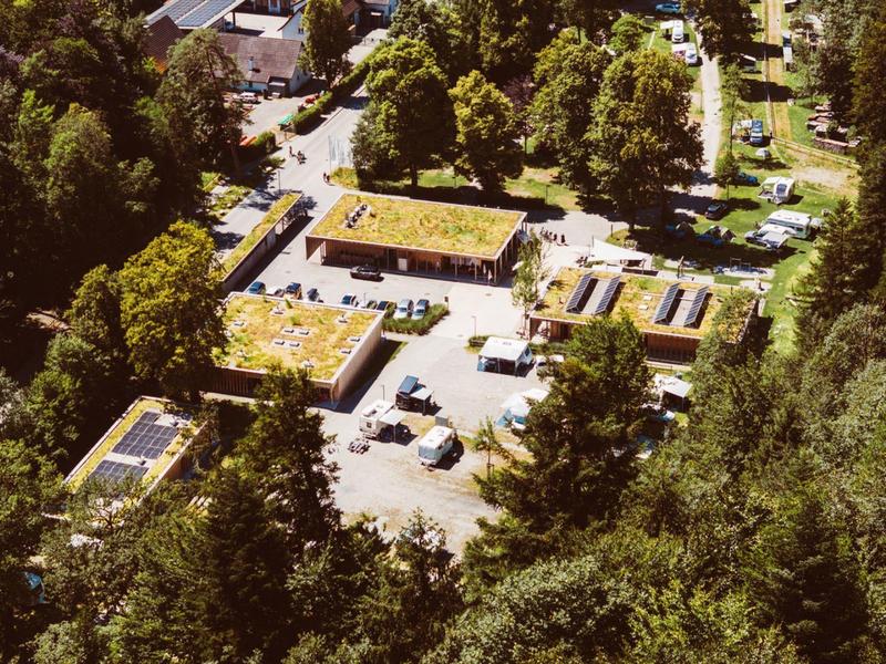 Aerial view of a hotel complex with green roofs, surrounded by dense forest.