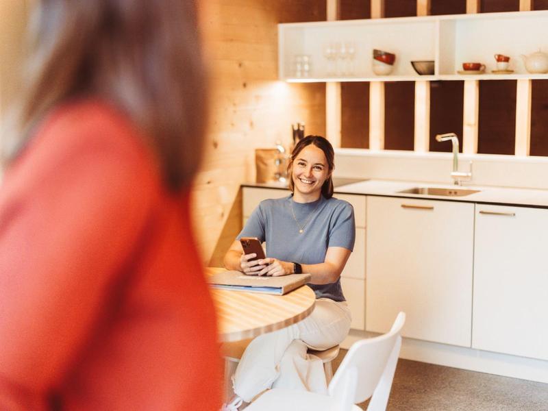 Woman sitting at table in modern kitchen smiling at another person.