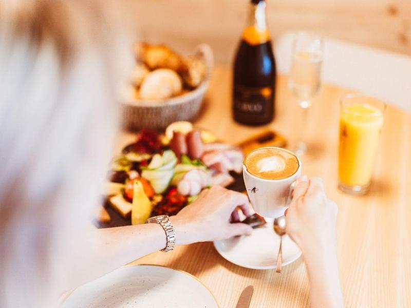 Woman holding cappuccino in café setting with breakfast and orange juice.