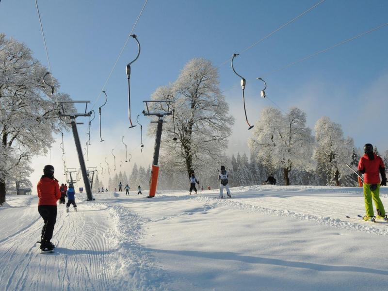 Skiers in colorful winter clothing on snowy slope with chairlift and snow-covered trees
