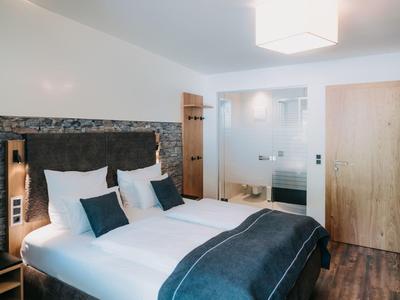 Modern hotel room with double bed, gray pillows, wooden doors, and hardwood floor.