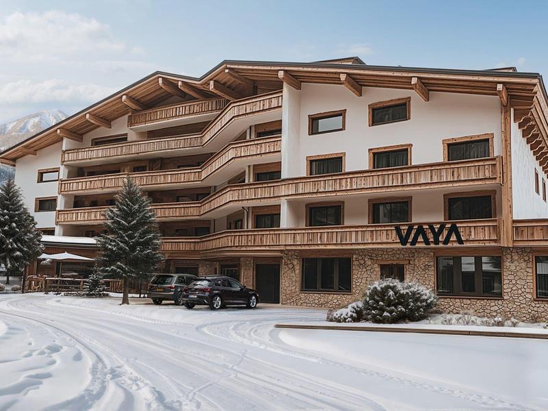 Modern alpine-style hotel building with wooden cladding and snow in the foreground.