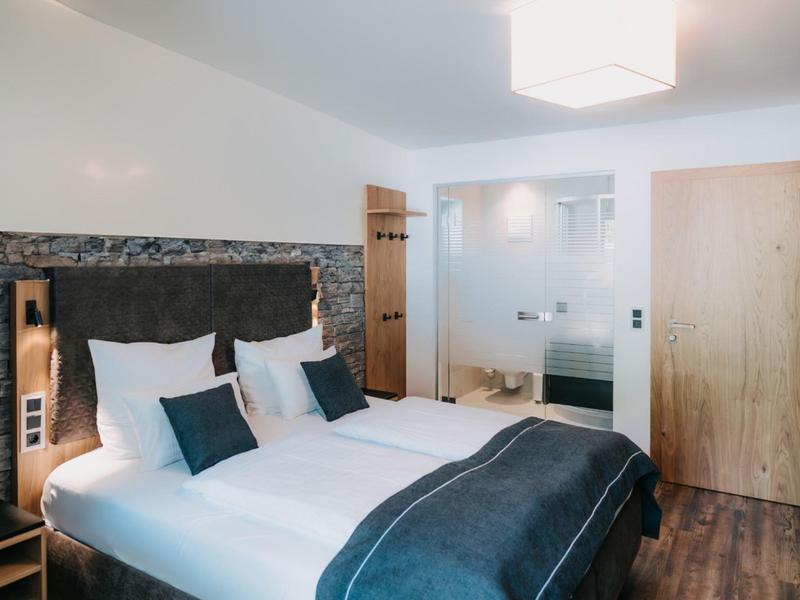 Modern hotel room with double bed, gray pillows, wooden doors, and hardwood floor.
