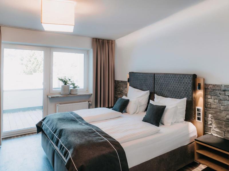Modern hotel room with double bed, window with curtains, and bedside tables.