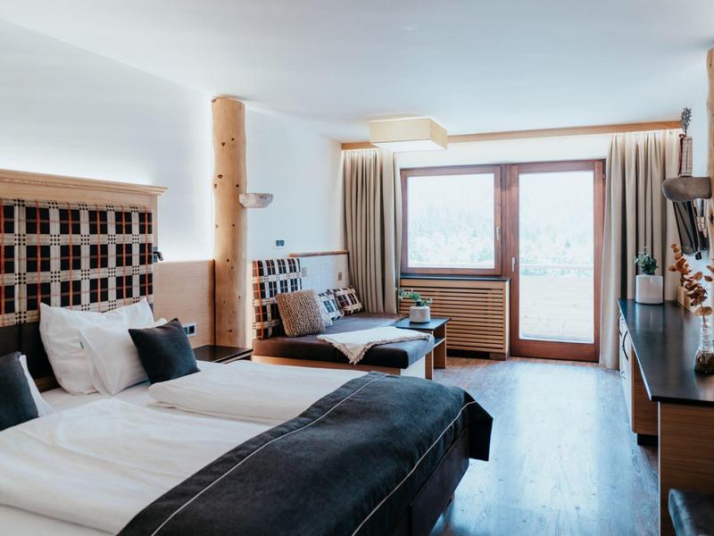 Modern hotel room with two beds, desk, and large window with curtains.