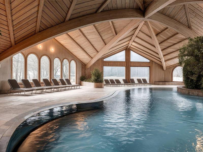Indoor pool with wooden beams ceiling, lounge chairs, and panoramic windows overlooking the lake.