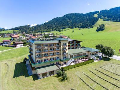 Hotelgebäude mit Terrasse und Pool in einer grünen Berglandschaft bei Sonnenschein.
