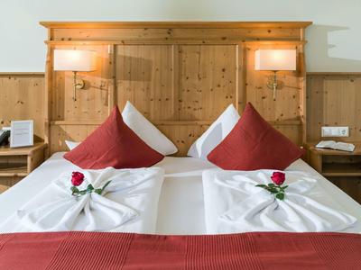 Two single beds with white linens, red pillows, and a red rose on each wooden headboard