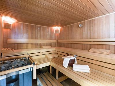 Sauna room with wooden walls, multi-level benches, and a sauna stove with stones.
