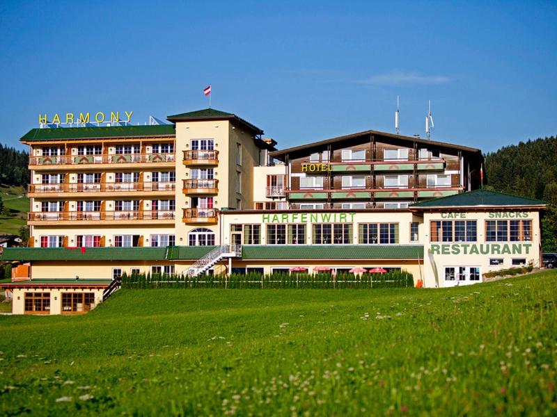 Large multi-story hotel with restaurant, surrounded by green meadow and hills.