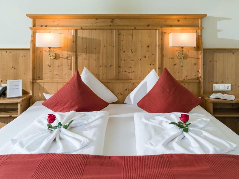 Two single beds with white linens, red pillows, and a red rose on each wooden headboard