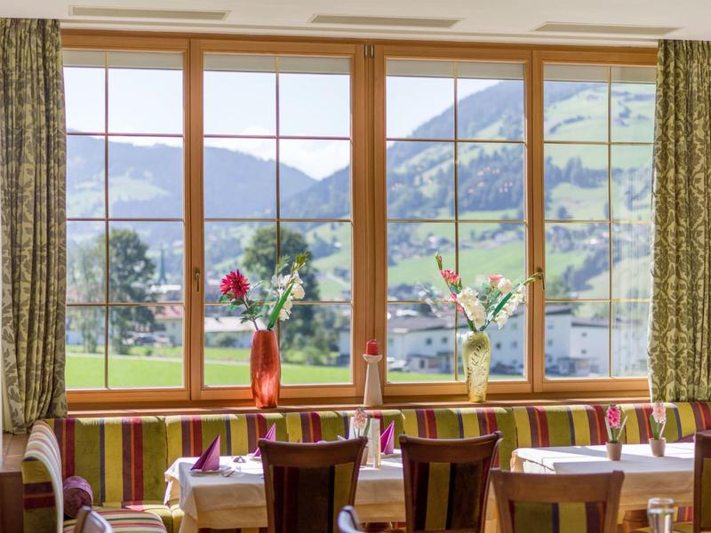 Cozy restaurant room with wooden tables, colorful chairs, and mountain view through large windows.