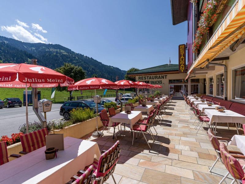 Hotel terrace with tables, chairs, and umbrellas set against a mountain backdrop.