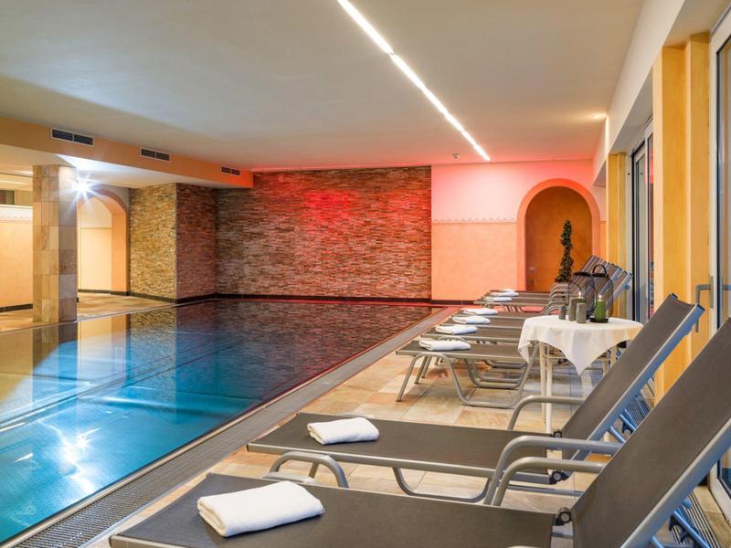 Indoor pool area with lounge chairs, towels, and modern lighting in a hotel.