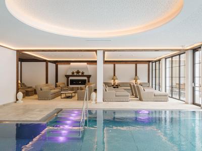 Piscina interna moderna con aree lounge e grandi finestre per luce naturale.