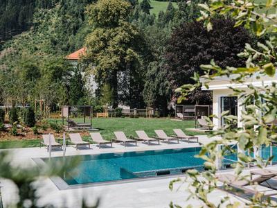 Pool mit Liegestühlen und grüner Landschaft im Hintergrund an einem sonnigen Tag