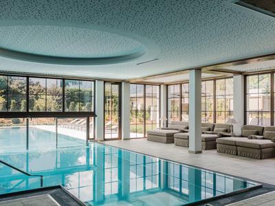 Piscina coperta luminosa con grandi finestre e aree relax confortevoli con vista esterna.
