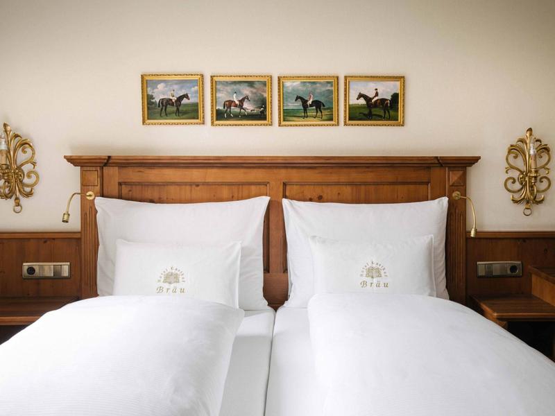 Camera d'hotel luminosa con due letti singoli, testiera in legno, biancheria bianca e decorazioni murali.