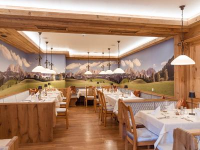 Restaurant confortable avec mobilier en bois, tables blanches et une fresque murale de panorama montagneux.