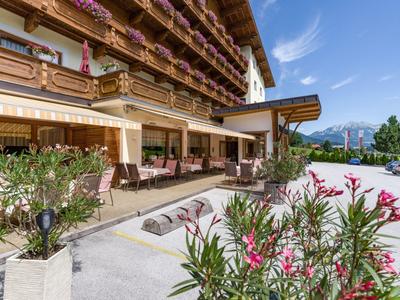 Terrasse d'hôtel avec sièges couverts, décorations florales et vue sur la montagne par ciel clair.