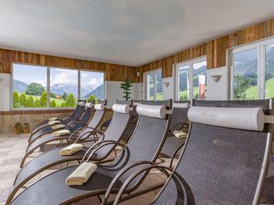 Ontspanningsruimte met ligstoelen en panoramische ramen met uitzicht op groene heuvels in een hotel.