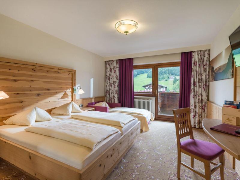 Lichte hotelkamer met twee eenpersoonsbedden, houten meubels en balkon met uitzicht op groene omgeving.