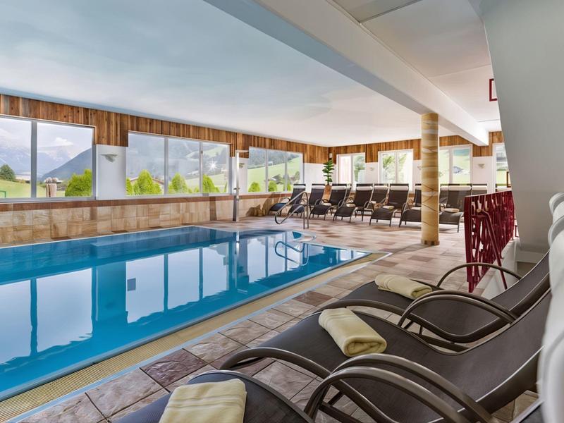 Binnenzwembad met ligstoelen en grote ramen met uitzicht op bergen in een hotel