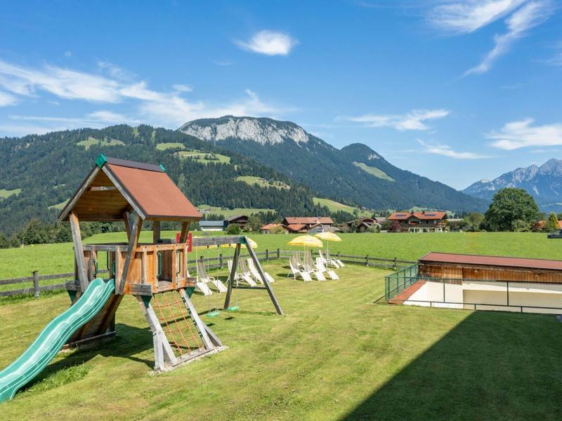 Grote tuin met speeltuin, glijbaan en bergzicht op een zonnige dag