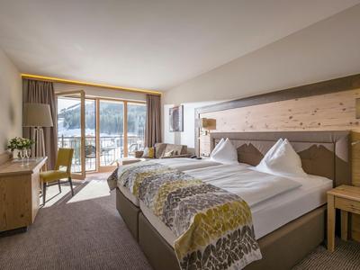 Licht ingericht hotelkamer met tweepersoonsbed, balkon en uitzicht op de bergen.