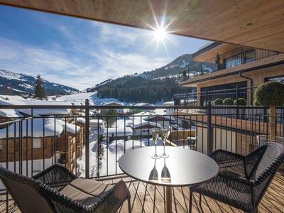 Balcon avec vue sur des montagnes enneigées, des bâtiments en bois et le soleil.