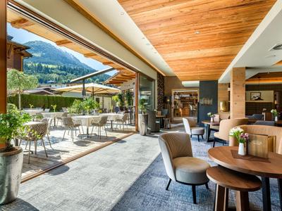 Moderne hotel eetruimte met uitzicht op terras en bergen, gezellige zitplaatsen en houten plafondbalken.