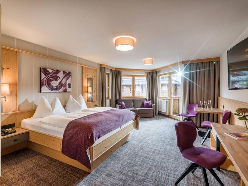 Camera d'hotel moderna con letto grande, area salotto e scrivania in tonalità calde.