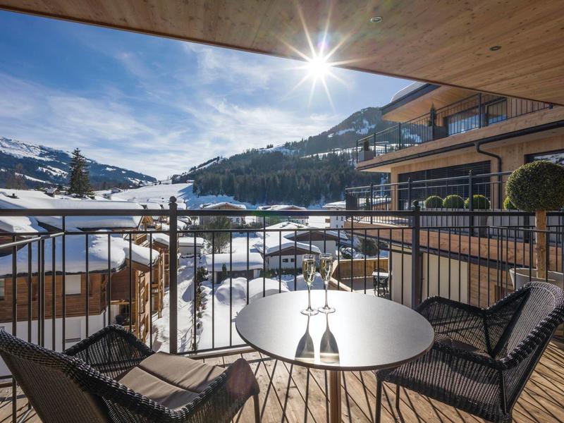Balcone con vista su montagne innevate, edifici in legno e sole.