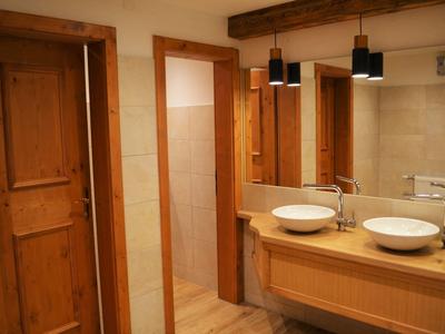 Łazienka z dwiema umywalkami, drewnianą szafką i drewnianymi drzwiami, ciepłe oświetlenie.