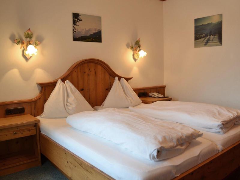 Łóżko podwójne z drewnianym zagłówkiem i szafkami nocnymi w prosto urządzonym pokoju hotelowym.