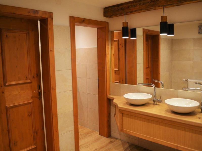 Łazienka z dwiema umywalkami, drewnianą szafką i drewnianymi drzwiami, ciepłe oświetlenie.
