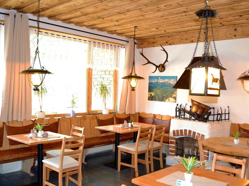 Jasna restauracja z drewnianymi meblami, kominkiem i dużymi oknami z roślinami.