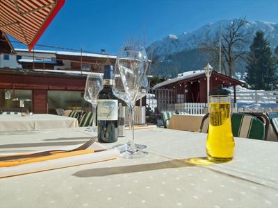Table with wine, glasses, and drink on terrace in front of snowy mountains on a sunny day.