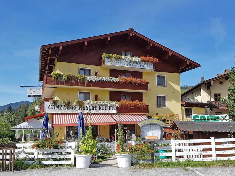 Yellow hotel with balconies, terrace, and garden in sunny weather.