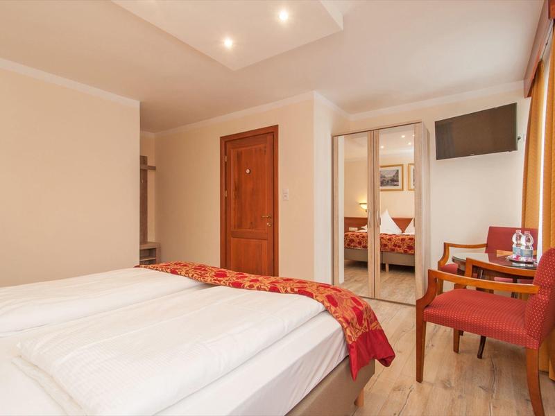 Hotel room with double bed, two chairs, a table, and a wall-mounted TV.