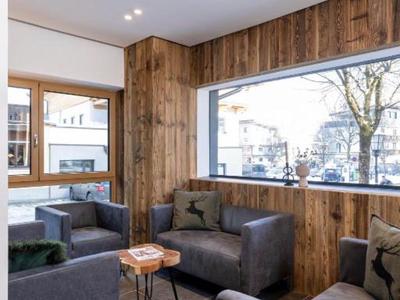 Moderne Hotellounge mit grauen Sesseln, Holzwänden und großem Fenster mit Straßenblick.