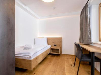 Kleines Hotelzimmer mit Einzelbett, Holzfußboden, Schreibtisch und Fenster mit Vorhang