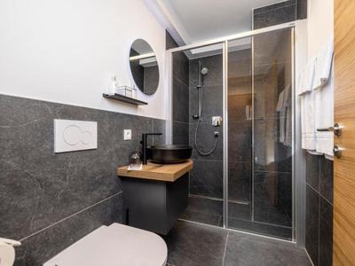 Modernes Badezimmer mit grauen Fliesen, Dusche mit Glastür, Waschbecken und WC in einem Hotelzimmer.