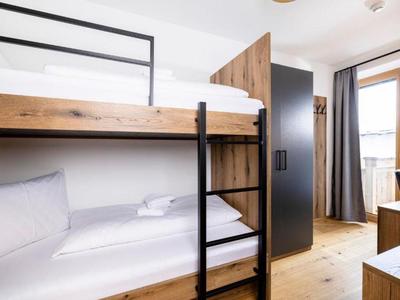 Modernes Hotelzimmer mit Etagenbett, Holzfußboden und Balkon mit Gardinen.