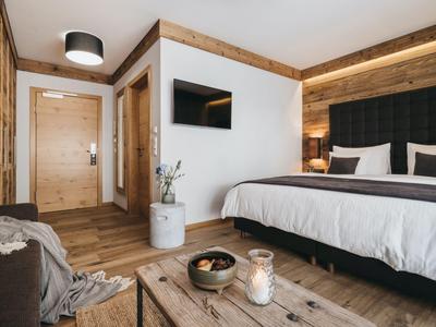 Modernes Hotelzimmer mit Doppelbett, Holzboden, TV an der Wand und rustikalem Holzdekor.