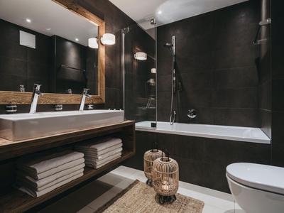 Modernes Badezimmer mit dunklen Wänden, Badewanne, Doppelwaschbecken und dekorativen Laternen.